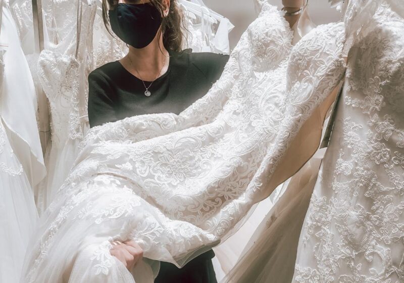 lace wedding dress on display with bridal stylist wearing mask